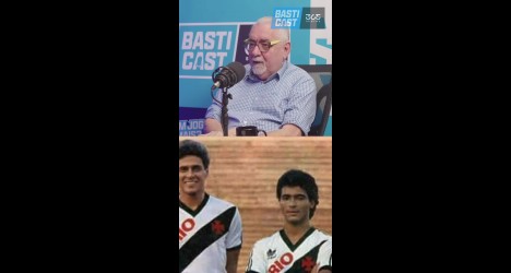 Homem falando em microfone com convidados ao fundo.