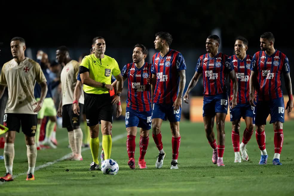 20250925-113953-1-16-arbitro-mostra-cartao-vermelho-para-jean-lucas-em-vasco-x-bahia-foto-jorge-rodriguesagif-1 Jogadores do Vasco e árbitro em campo durante partida no estádio.