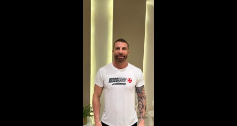 Homem com camisa branca e tatuagem visível.