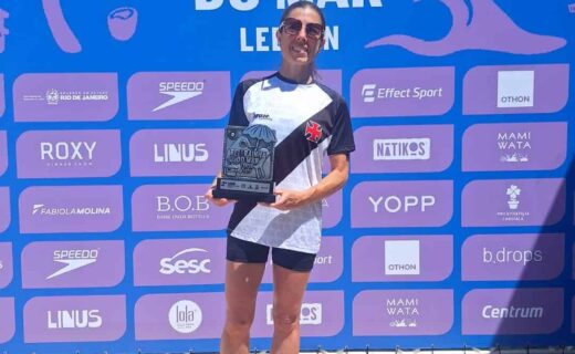 Corredora segurando troféu na praia, após corrida de revezamento.