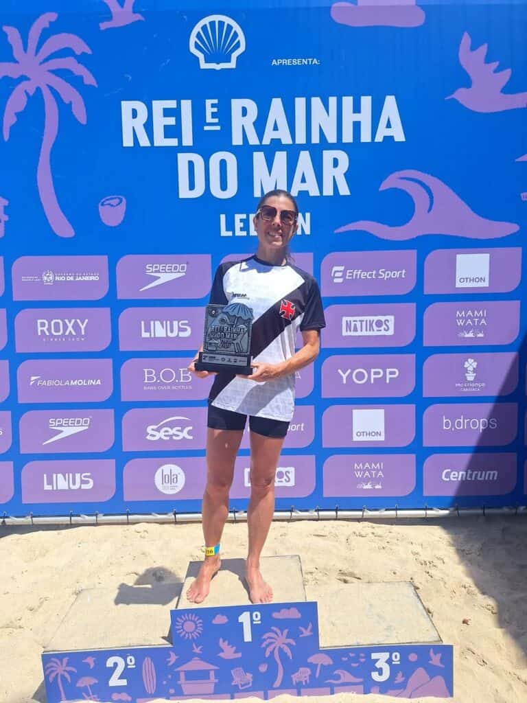 Corredora segurando troféu na praia, após corrida de revezamento.