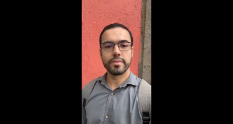 Homem com óculos e mochila against parede coral.