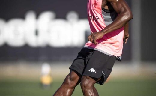 Jogador de futebol treinando com a bola no campo.