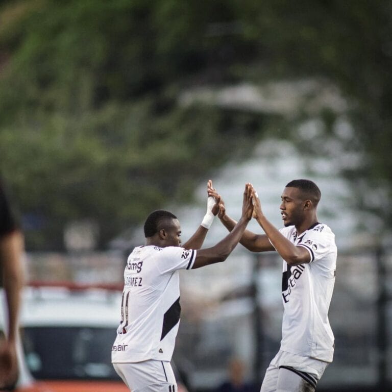 Jogadores comemorando gol, trocando high five em campo de futebol.