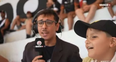 Locutor com microfone e menino sorridente em estádio.
