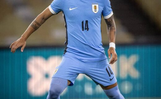 14 jogador com uniforme azul, chuteira roxa, jogando futebol.