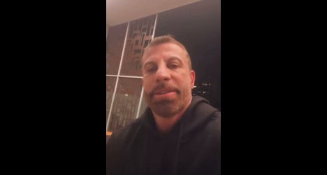 Homem com barba e hoodie escuro em ambiente interno.