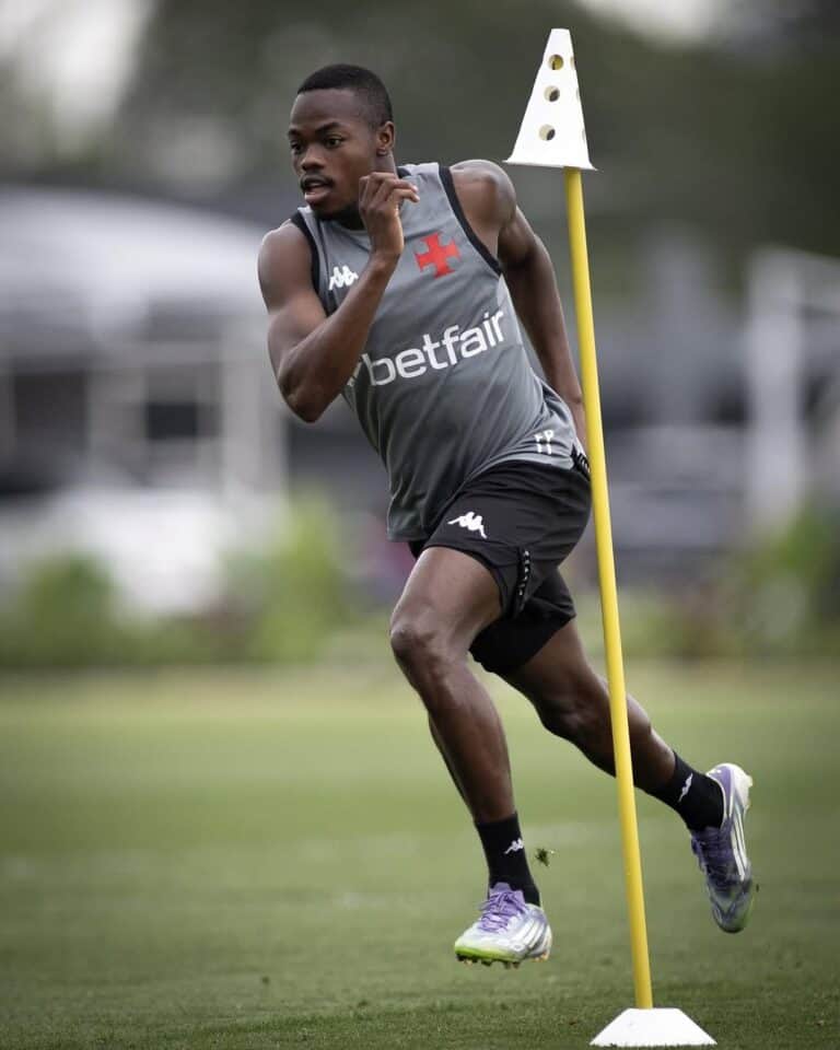 Atleta masculino treinando corrida com cones em campo ao ar livre.