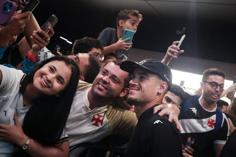 Fã sorridente com camisa do Vasco em evento com outros torcedores.