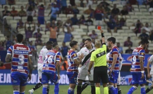Pessoas jogando futebol no estádio com árbitro mostrando cartão vermelho.