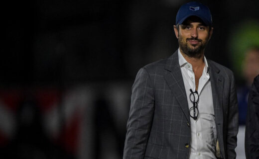 Vasco da Gama treinador em campo com traje formal e boné azul.