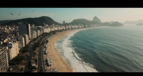 Vista aérea da orla de Copacabana, Rio de Janeiro, com o mar, praia e edifícios ao fundo.