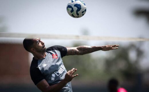 Bola de futebol no ar com jogador ao fundo.