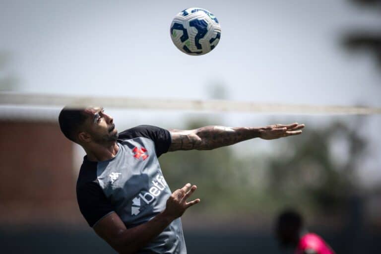 Bola de futebol no ar com jogador ao fundo.
