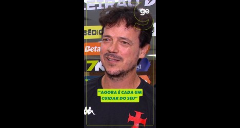 Homem com camiseta preta e fundo de banners esportivos.