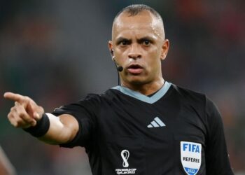 Árbitro de futebol apontando, uniforme preto com logotipos FIFA e Mundial 2022.