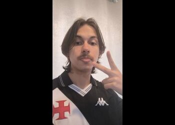 Jovem com cabelo longo e barba, fazendo gesto de paz.