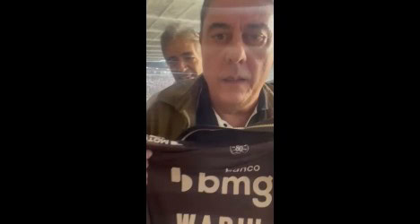 Homem falando ao celular com fundo de pessoas.