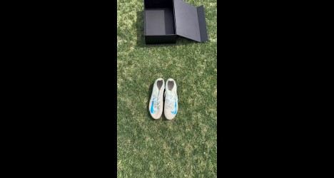 Tênis branco com detalhes azuis sobre grama verde.