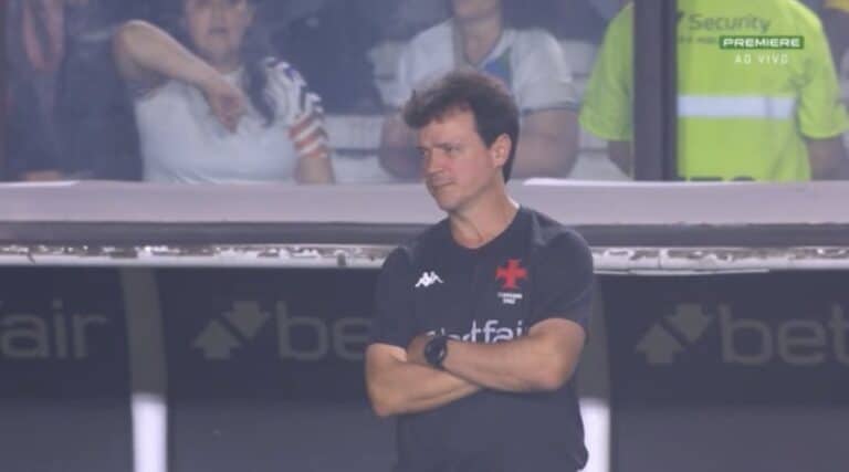 Treinador do Vasco em campo, com braços cruzados, olhar sério, usando camiseta preta com logo do clube.