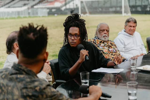 Mulher negra fala em reunião ao ar livre com microfone.
