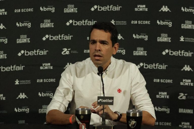 Jorge Salgado em coletiva de imprensa vestindo camisa branca com escudo do Vasco.