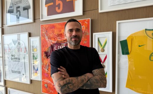 Vestido preto com braços cruzados em exibição de troféus e camisas de futebol.