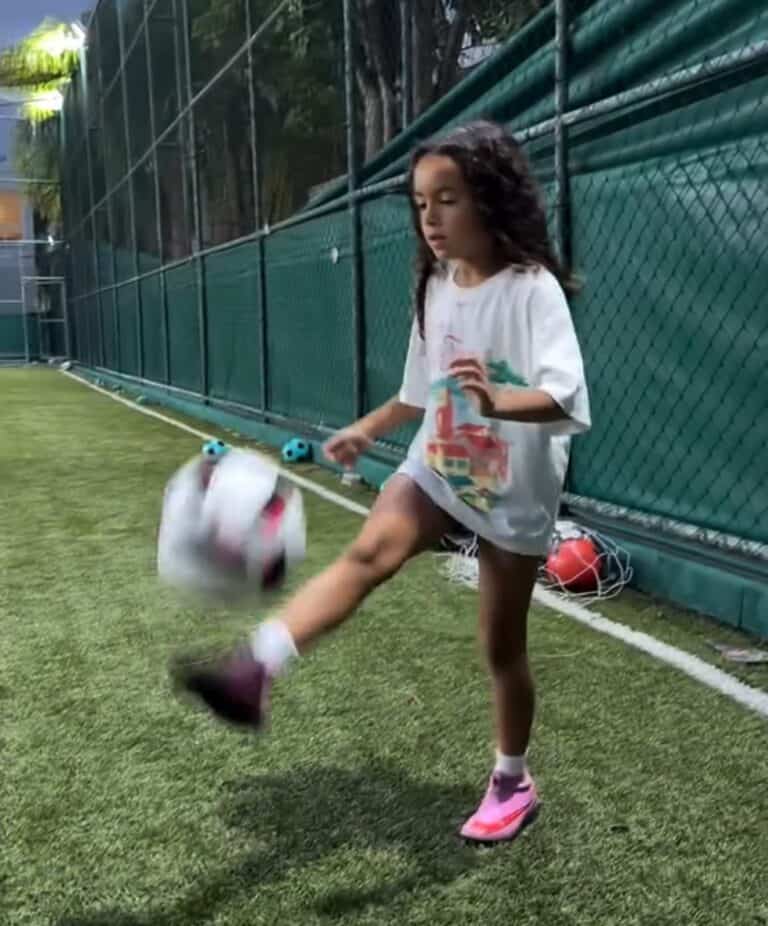 Bebê chutando bola de futebol no gramado.