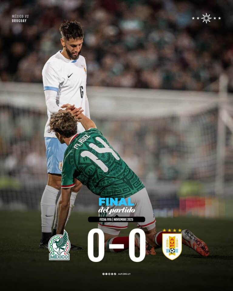 Jogador de futebol de perfil, com uniforme branco e azul, ajoelhado, apoiando a mão em um adversário no campo.