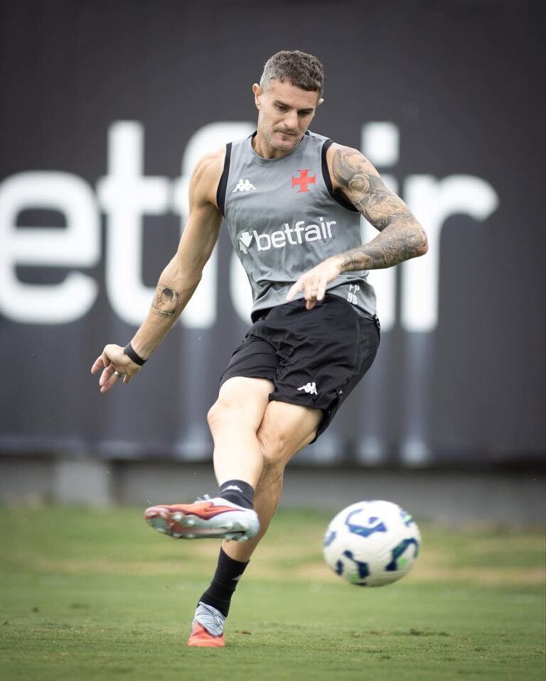 Jogador de futebol treinando com a bola no campo, vestindo uniforme cinza e preto.