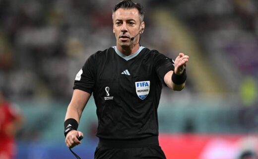 Árbitro de futebol com uniforme preto e crachá FIFA.