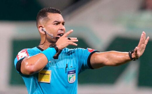 Árbitro de futebol com microfone e uniforme azul.