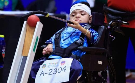 2. Criança com deficiência em cadeira de rodas segurando raquete de tênis de mesa.