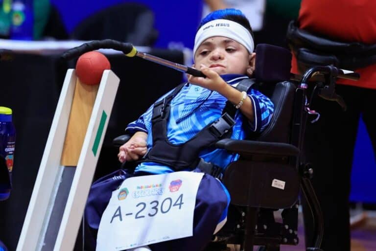 2. Criança com deficiência em cadeira de rodas segurando raquete de tênis de mesa.