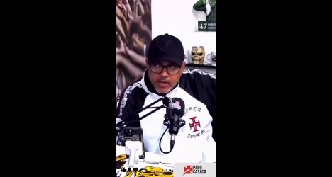 Homem com óculos e boné fala em microfone.