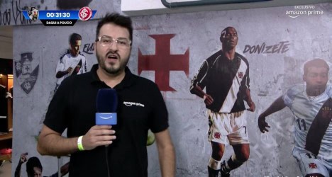Reportagem do Vasco na transmissão ao vivo, com apresentador falando na câmera, fundo com símbolos do clube e jogadores em destaque.