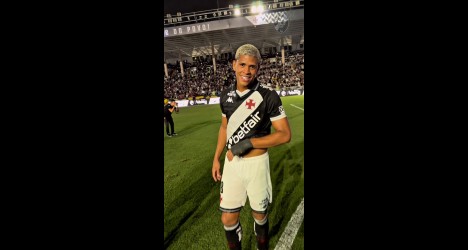 Jovem jogador do Vasco no estádio, sorrindo com uniforme preto e branco.