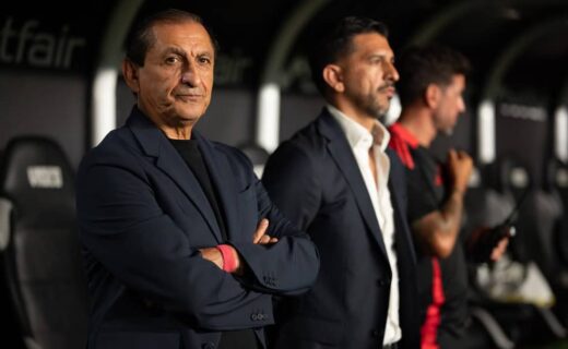 Treinador do Vasco com dirigentes ao lado, atentos durante partida no estádio. Ambiente de jogo, com foco na comissão técnica, destaque para expressão de concentração.