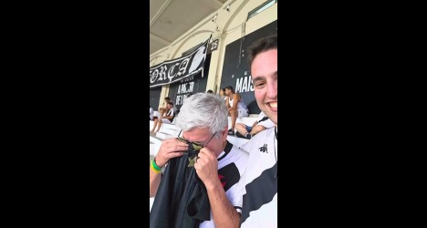 Homem sorrindo e segurando uma camiseta do Vasco, visivelmente emocionado, em um estádio lotado, celebrando um momento especial do clube.