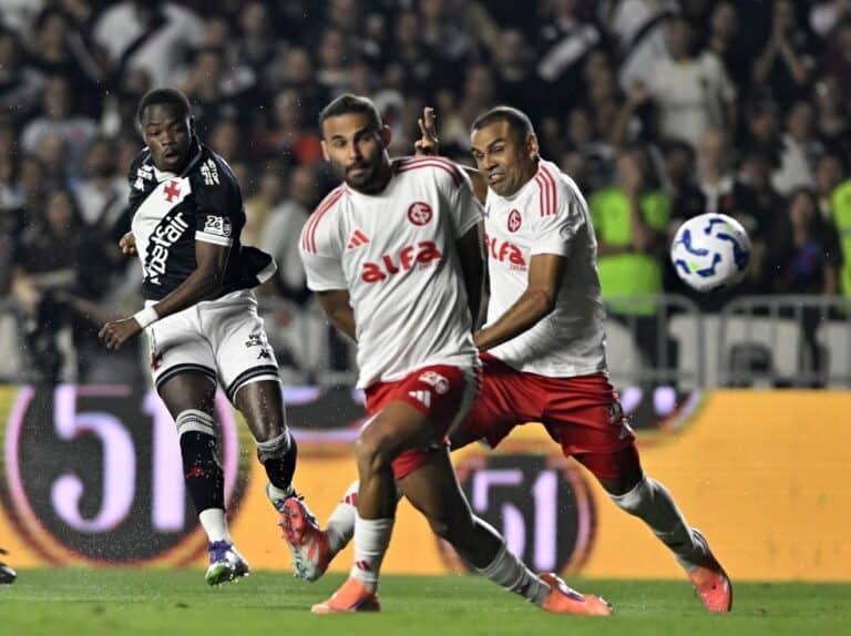 2. Alt: Jogadores do Vasco em ação durante partida de futebol, uniforme branco e vermelho, estádio cheio, clima de competição.