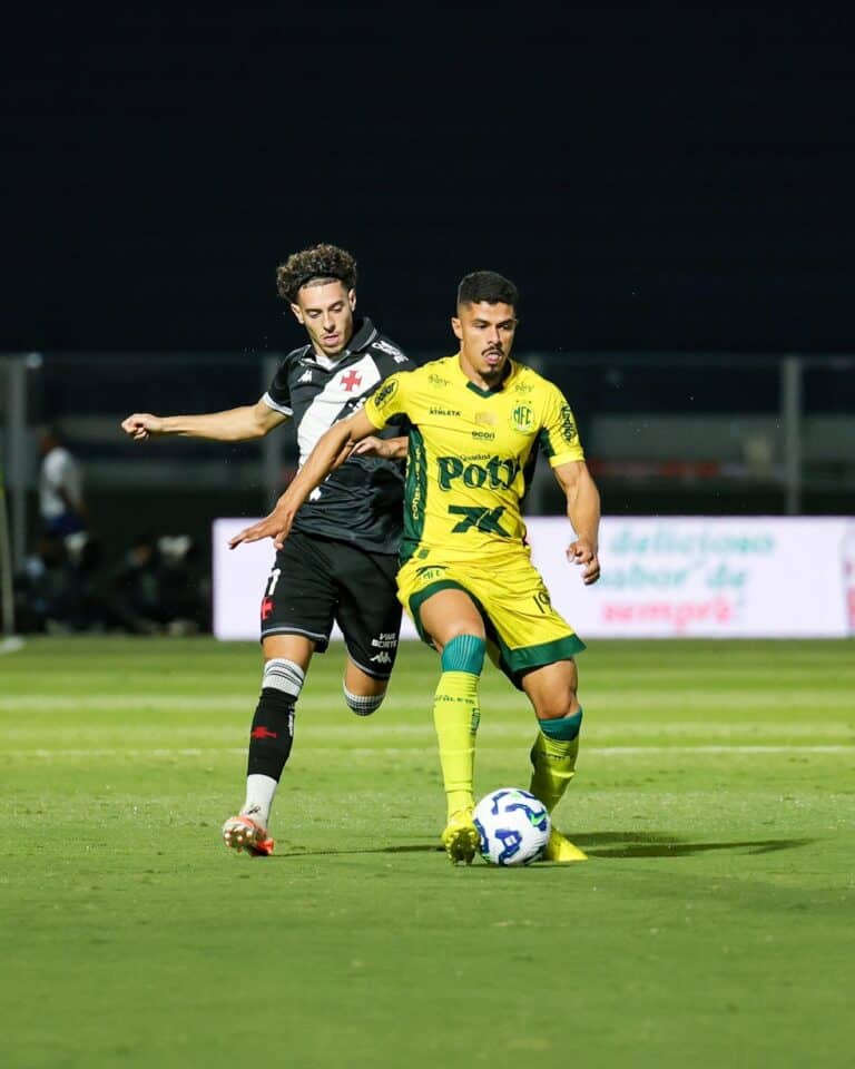 Atleta usando uniforme amarelo tenta controlar a bola, enquanto adversário de uniforme preto tenta interceptar.