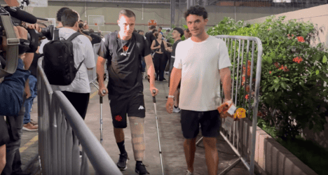 Vasco e torcedor no aeroporto, homem com muletas e mochila, ao fundo outras pessoas.