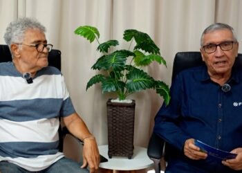 Homens conversando em ambiente interno com planta ao centro.